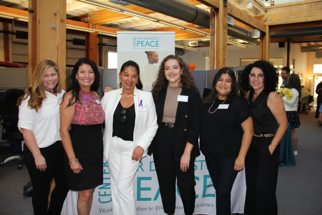 C4DP staff members pose together at an indoor gathering, standing in front of the organization’s banner while celebrating their work supporting survivors and preventing domestic violence in Marin County.