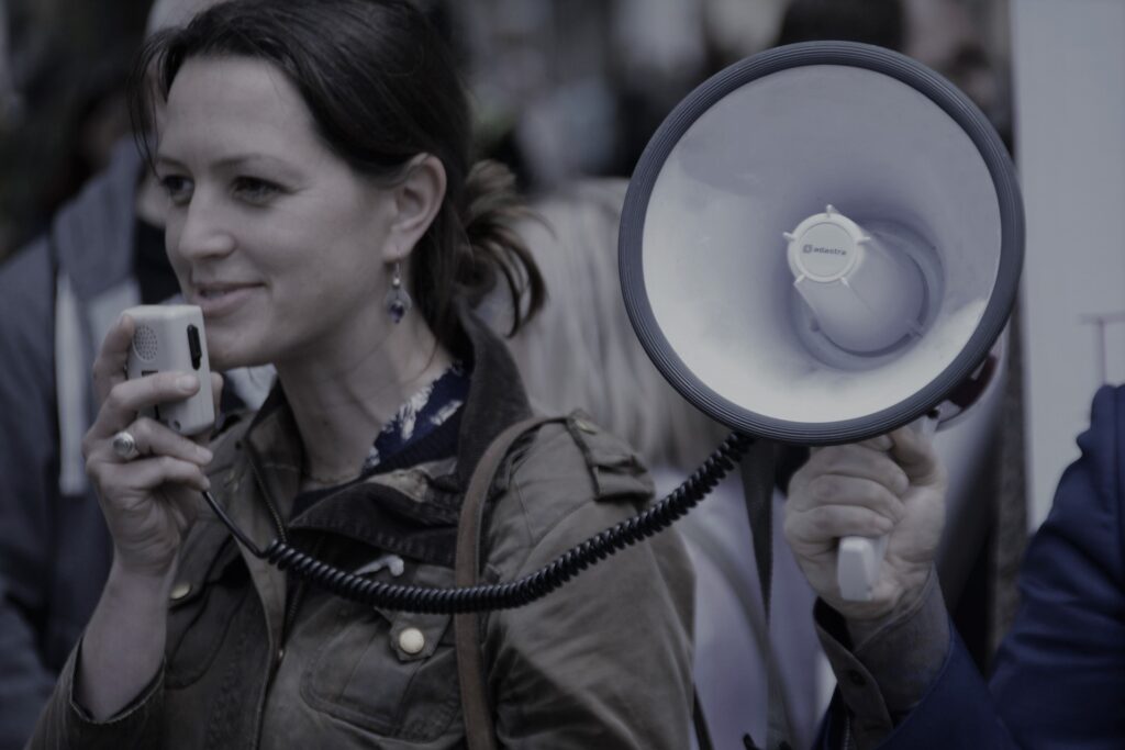 A woman speaks into a handheld microphone beside a megaphone during a public rally in Marin County advocating for action to end domestic violence.