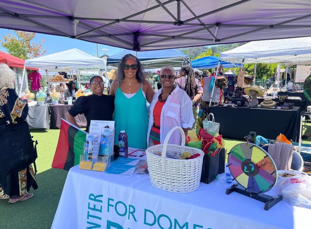 Three C4DP staff members stand behind an outreach table at a community event in Marin County, offering brochures and resources on domestic-violence prevention.