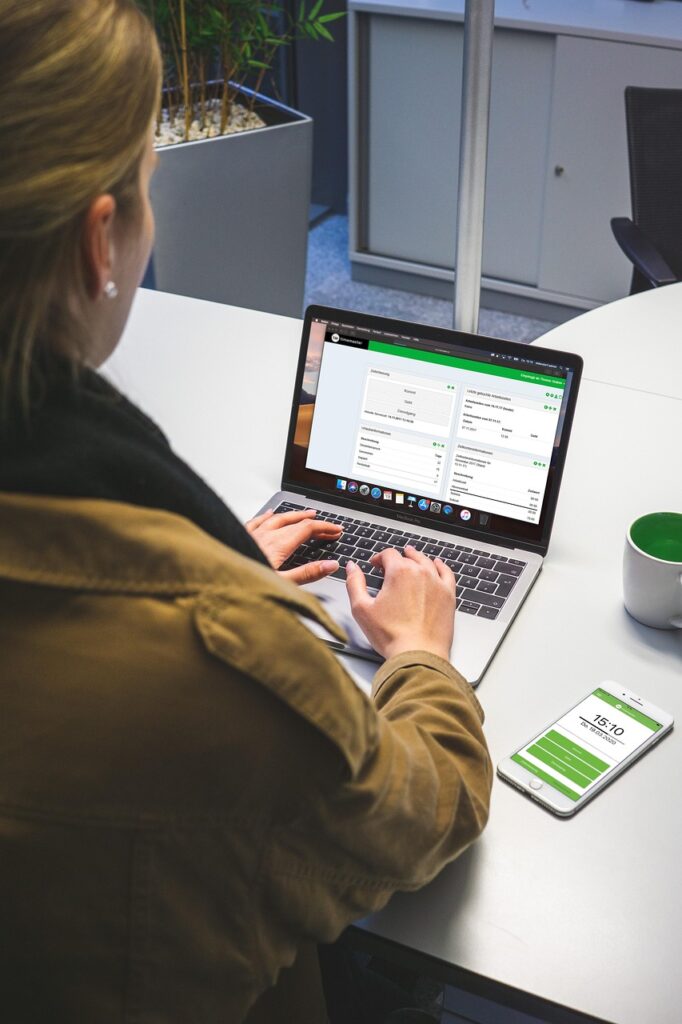 A person sits at a desk working on a laptop that displays an online dashboard, with a smartphone showing a matching interface beside them, representing digital tools used to support C4DP’s work.
