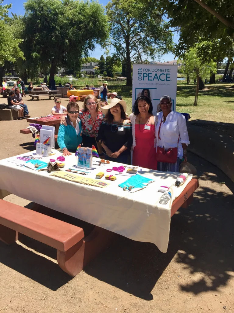 A group of C4DP representatives gather behind an outdoor resource table at a community event, sharing materials and information to support survivors and promote healthy, safe relationships.