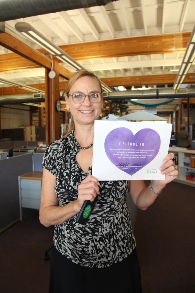 C4DP employee Marla holds a signed Purple Heart pledge in the office, affirming her commitment to speak up and take action to prevent domestic violence during DV Awareness Month.
