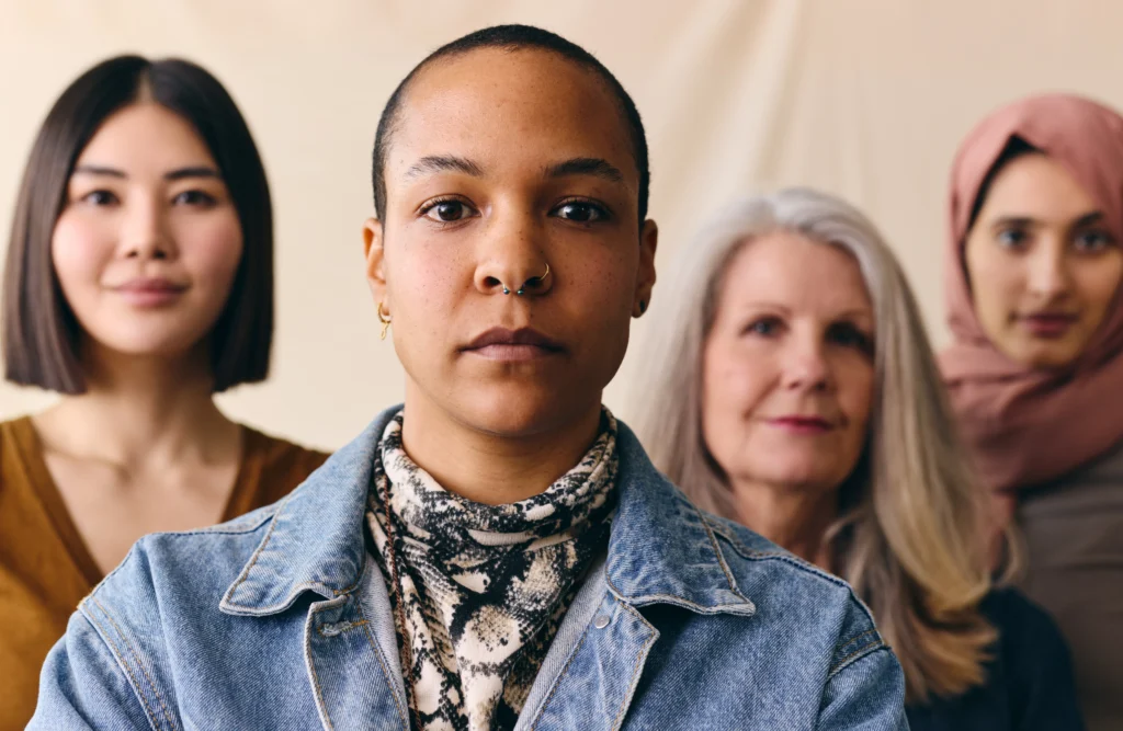 Portrait of four diverse women standing together, looking forward with a serious and determined expression.