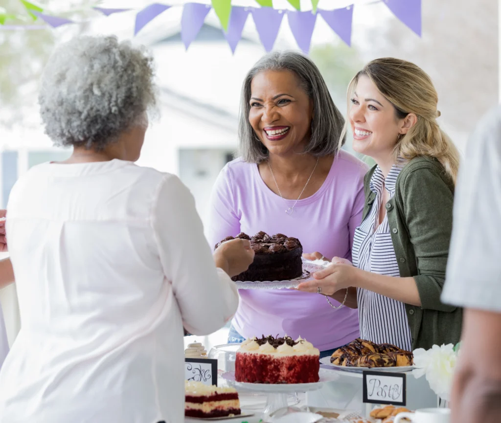 Women smile and serve cake together at a community bake-sale fundraiser, supporting programs that help end domestic violence in Marin County.